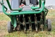 Green lawn aerator with rotating tines on grass.