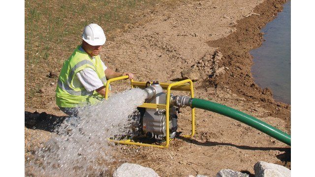 Person in safety vest operating a water pump, discharging water near a body of water.