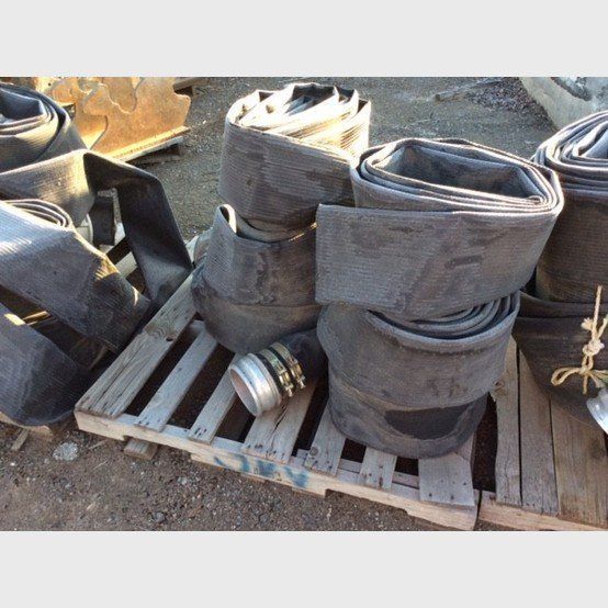 Black rolled-up rubber hoses stacked on a wooden pallet outdoors.