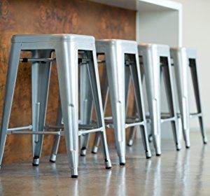 Five silver metal bar stools lined up against a copper-toned wall.