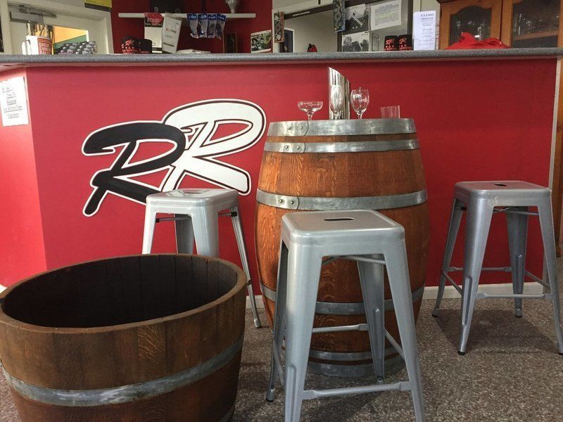 Bar area with red wall, barrel table, metal stools, and RR logo.