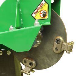 Green farm equipment with a metal disc and warning sign.