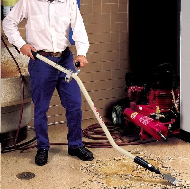 Man using a floor scraper attached to an air compressor to remove flooring.