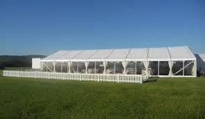 White tent with clear windows and a picket fence in a grassy field under a blue sky.