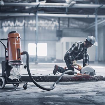 Construction worker using a saw, connected to a vacuum in a warehouse.