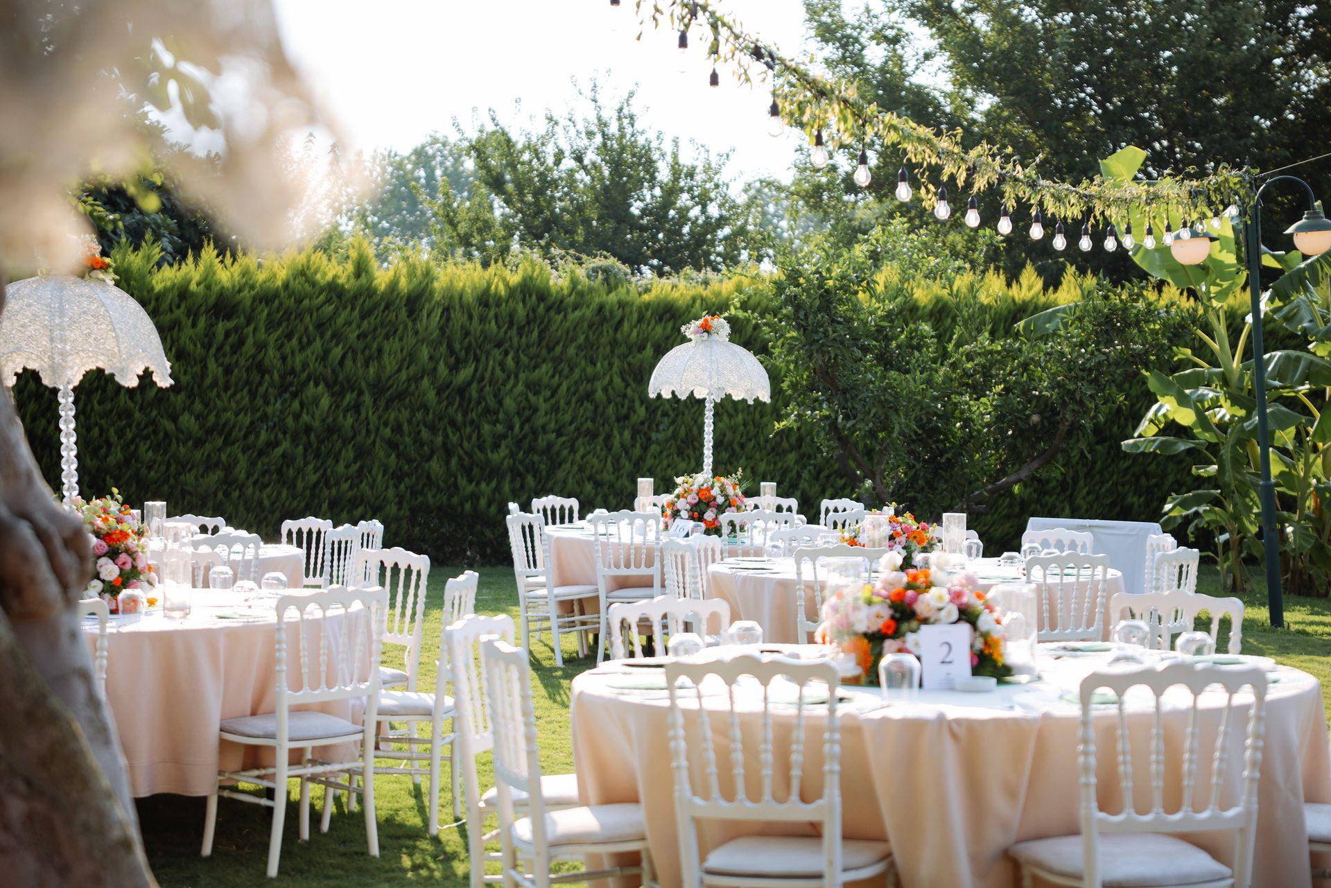 Wide view of an outdoor party set up, with white tables, chairs, and utensils.