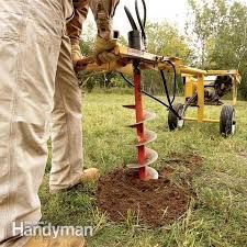 Person using a powered auger to drill a hole in the ground outdoors.