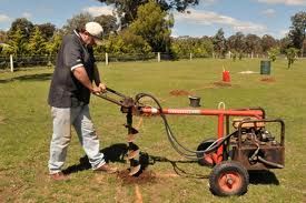 Man operating a motorized auger to dig a hole in a grassy field.