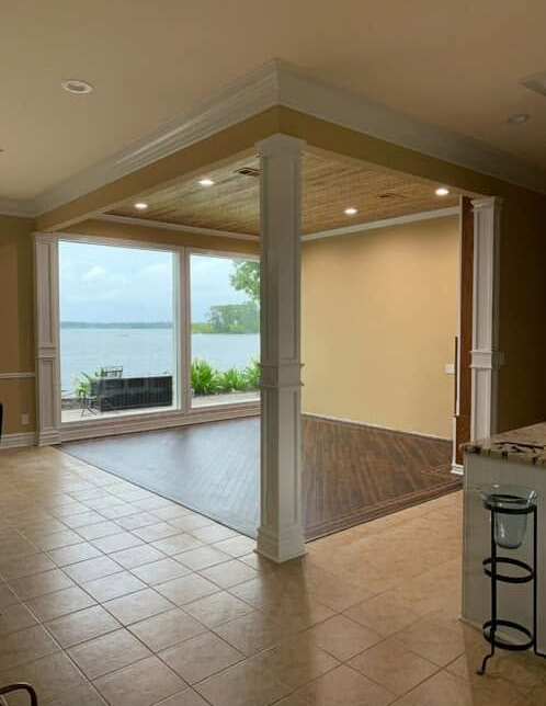Open living room with tiled floor and wood ceiling, overlooking a lake through large windows.