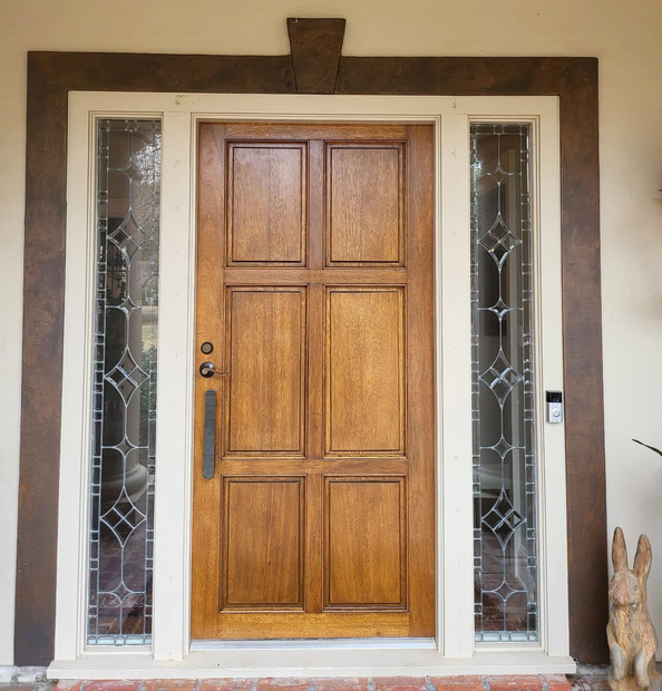 Wooden front door with narrow frosted glass sidelights in a stucco entryway