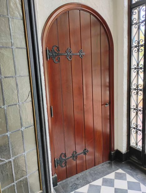 Wooden arched door with black iron hinges and handle beside patterned tile walls and floor