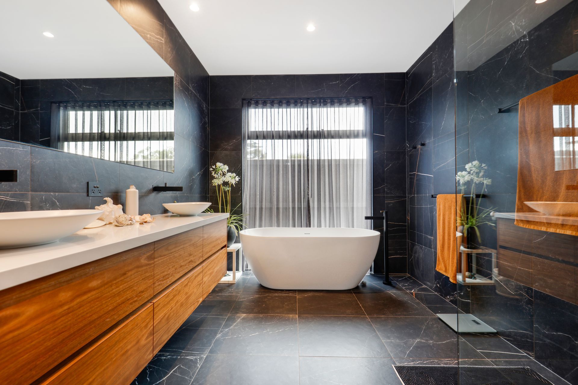 Modern bathroom with freestanding tub, double sink, dark tile, and large windows