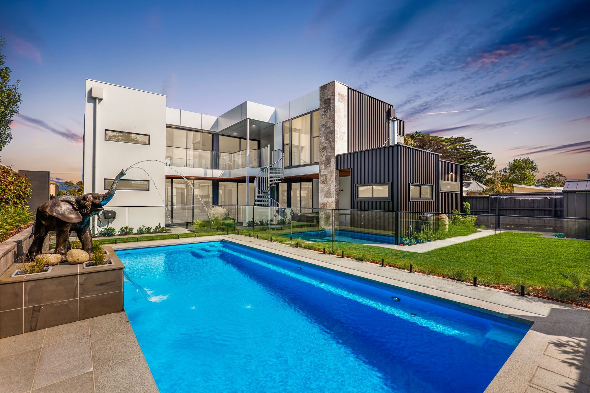Modern luxury home with a blue swimming pool and landscaped yard at dusk