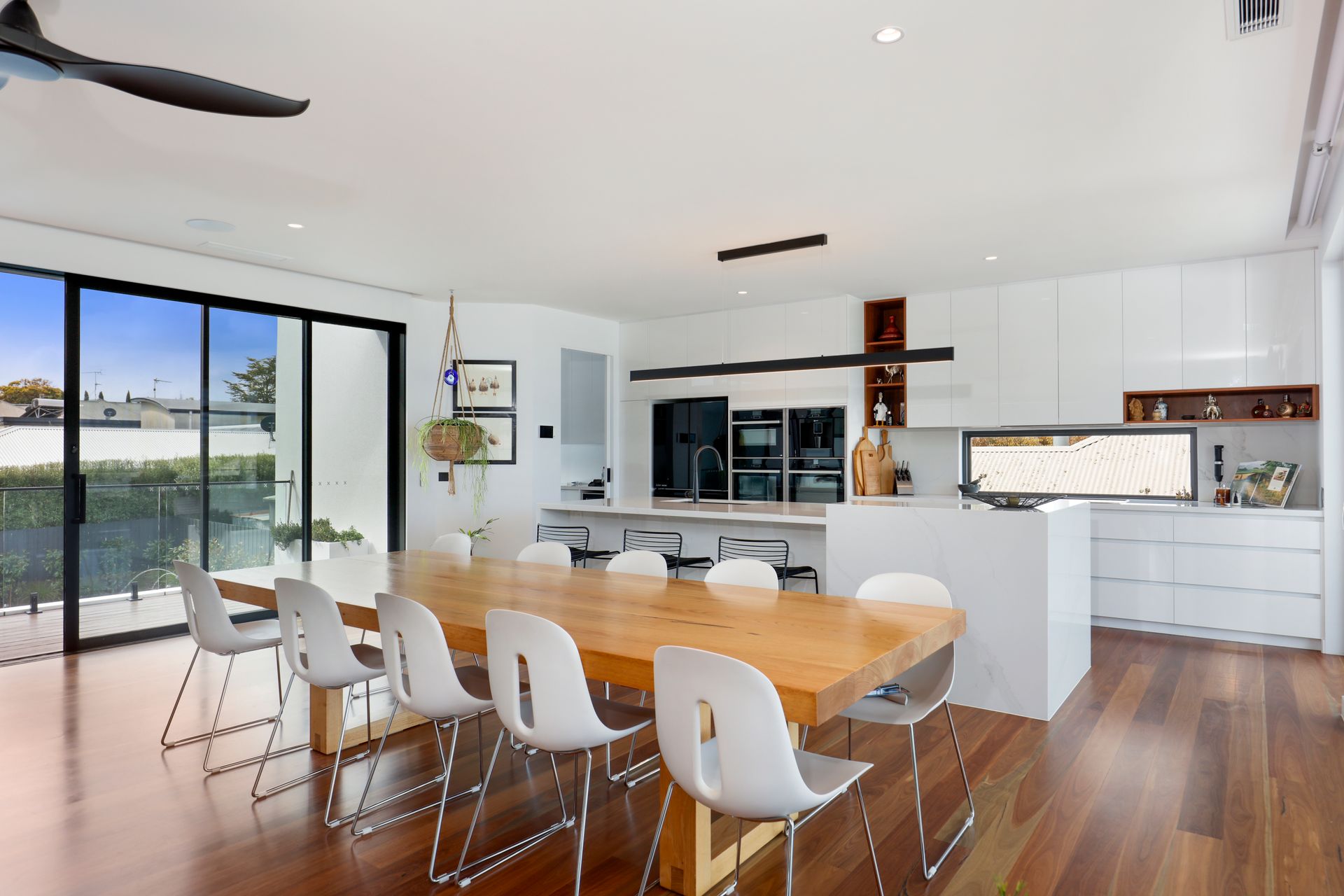 Modern open-plan kitchen and dining area with white chairs, wooden table, and sliding glass doors