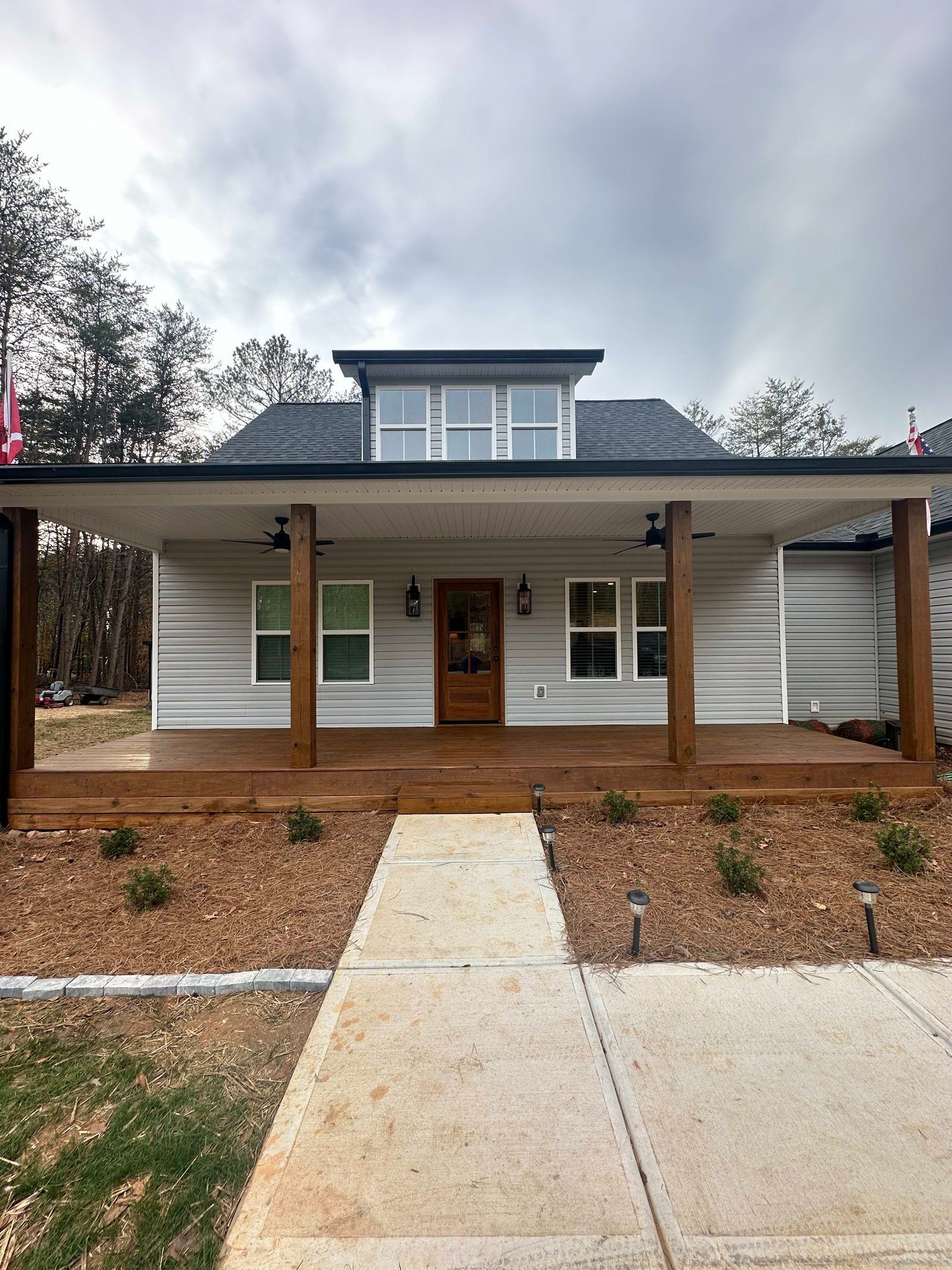Gray house with a porch and wooden columns, brown door, and walkway leading to the entrance.