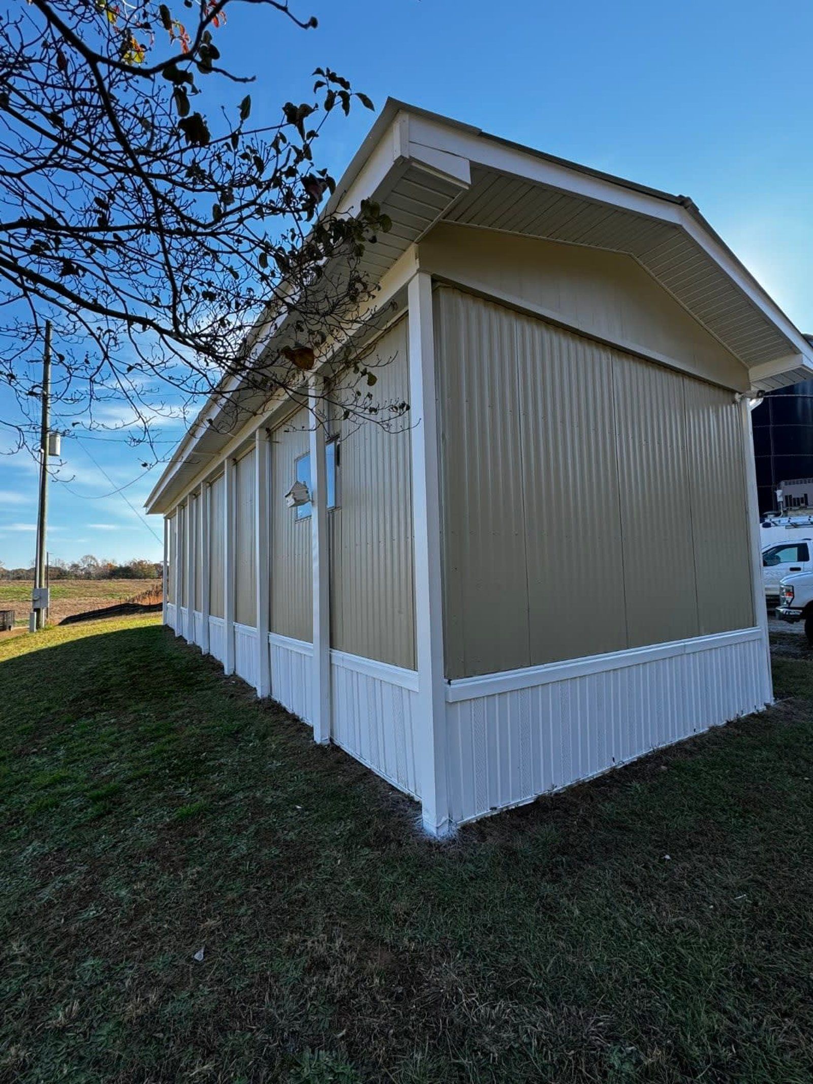 Tan and white building with a corrugated metal exterior. Overcast skies. Green grass, and tree branch in view.