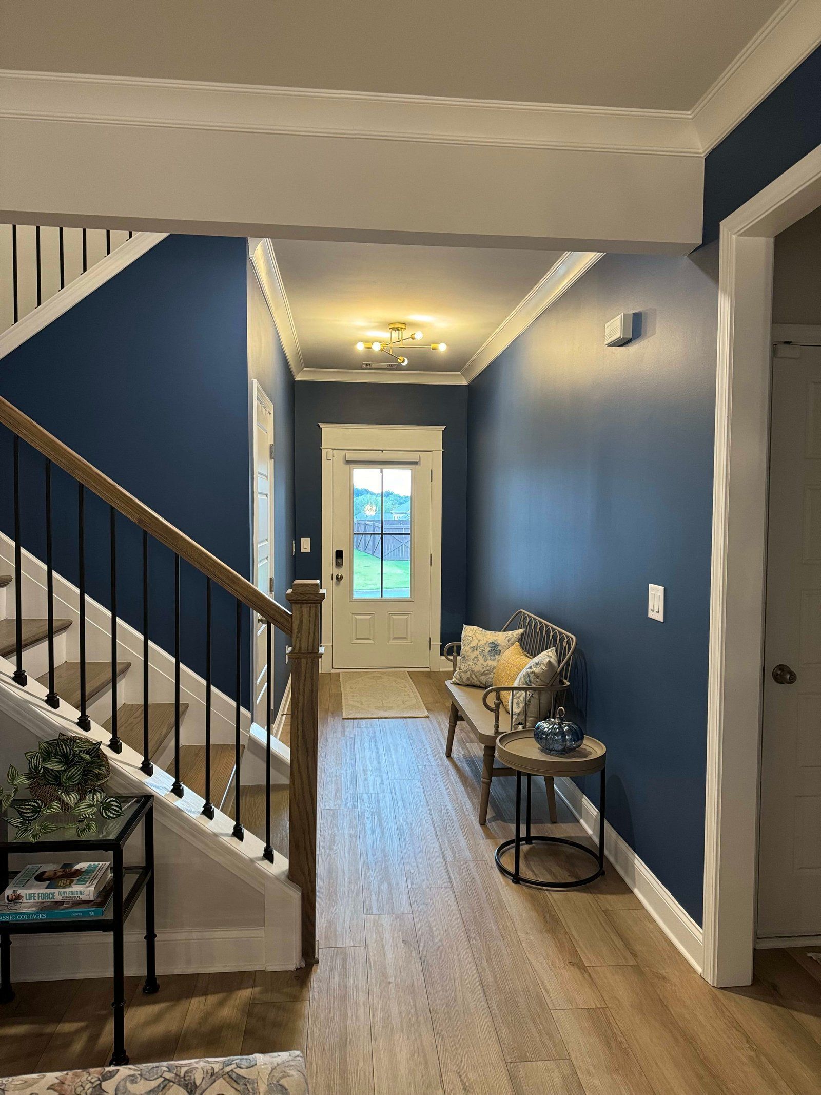 Blue hallway with a wooden staircase, door, and a bench.