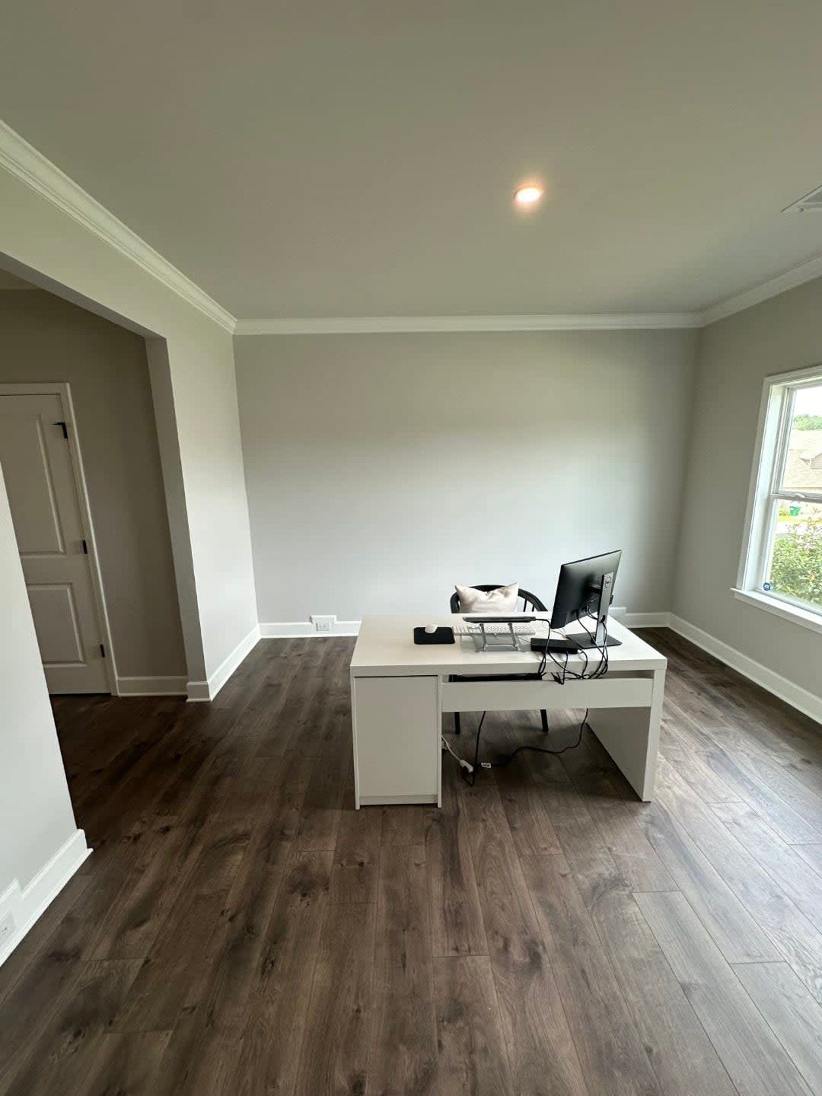 Empty room with a white desk, computer, and wood-look flooring. Light gray walls with white trim.