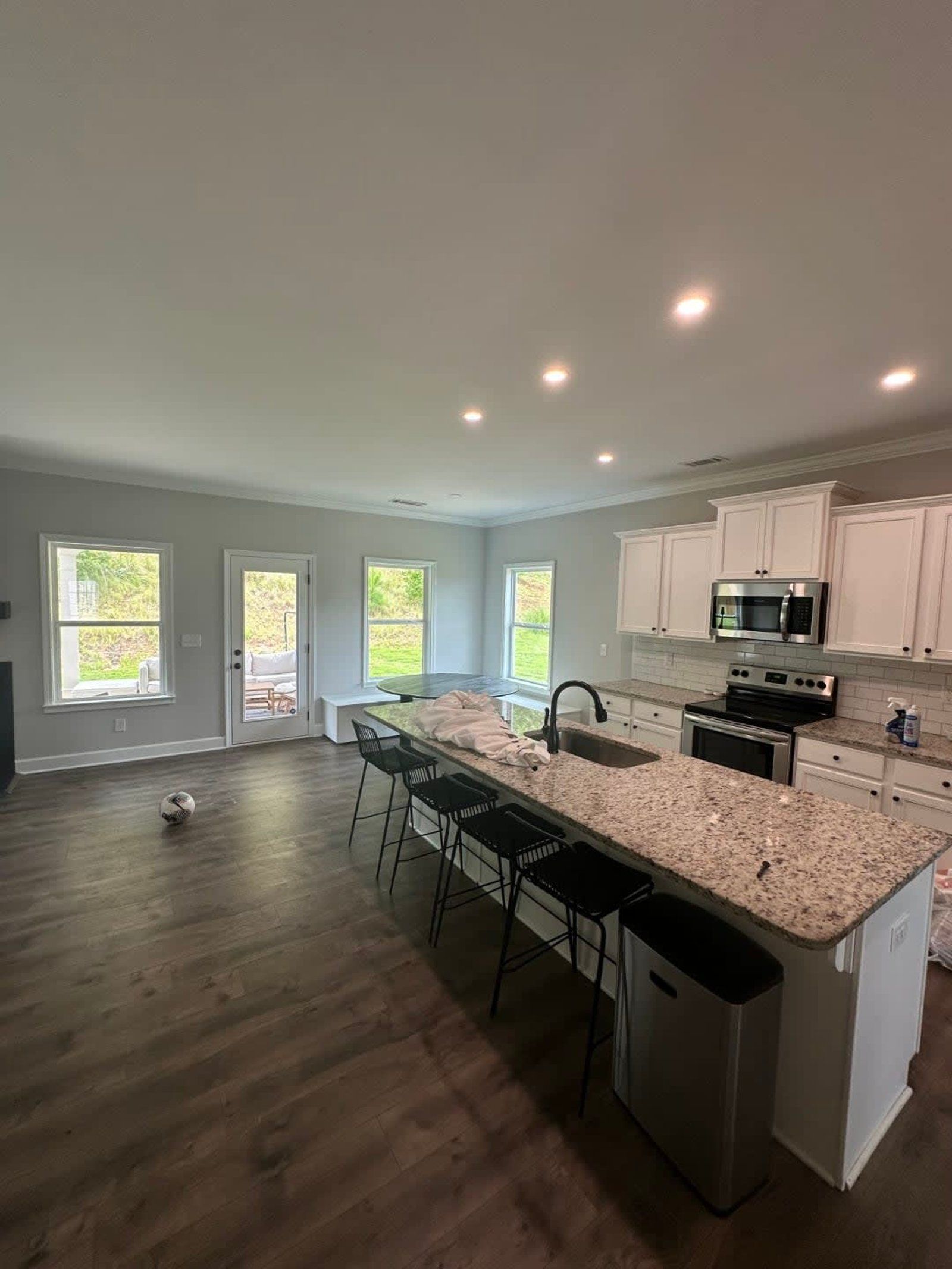 Open-concept kitchen with island and bar stools, granite countertop, white cabinets, and stainless steel appliances.