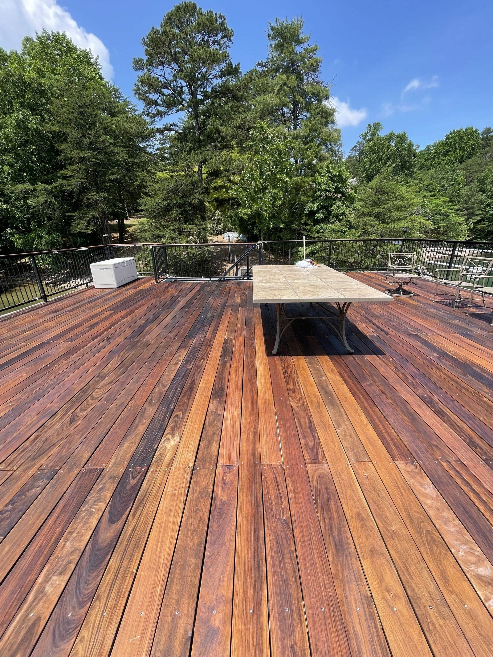 Wooden deck with built-in bench, trees in the background, blue sky.