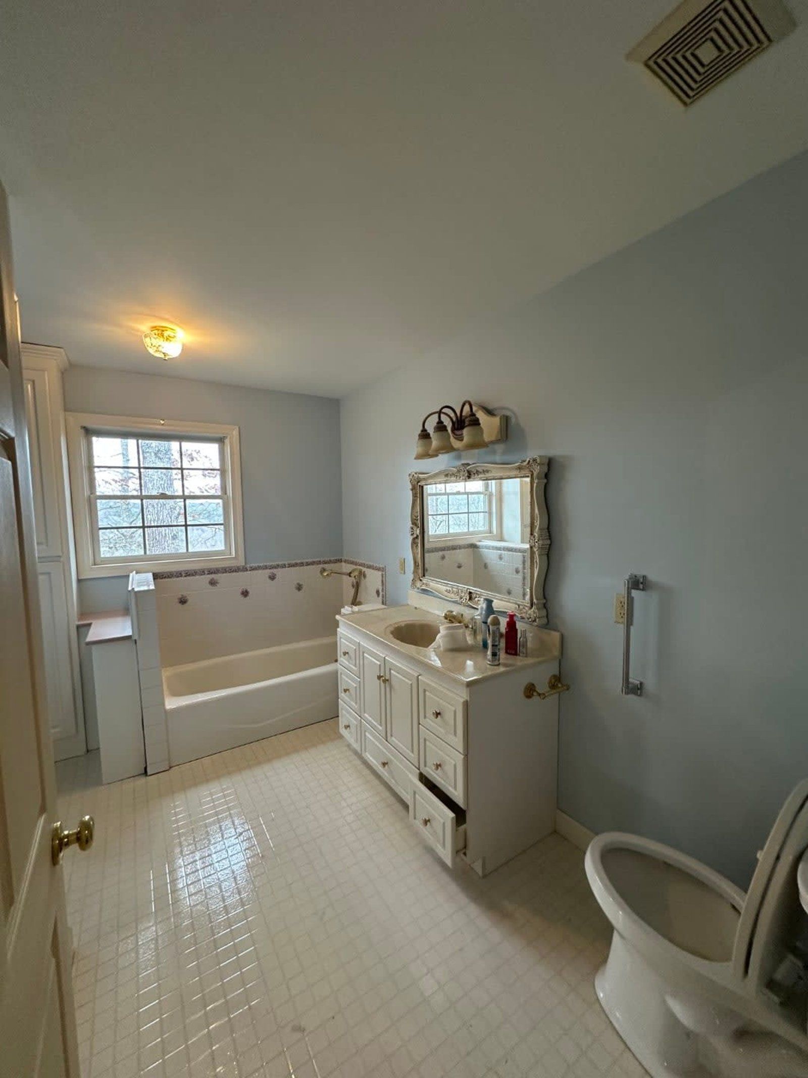 Bathroom with white tile floor, light blue walls, white vanity, and toilet. Bathtub with window.