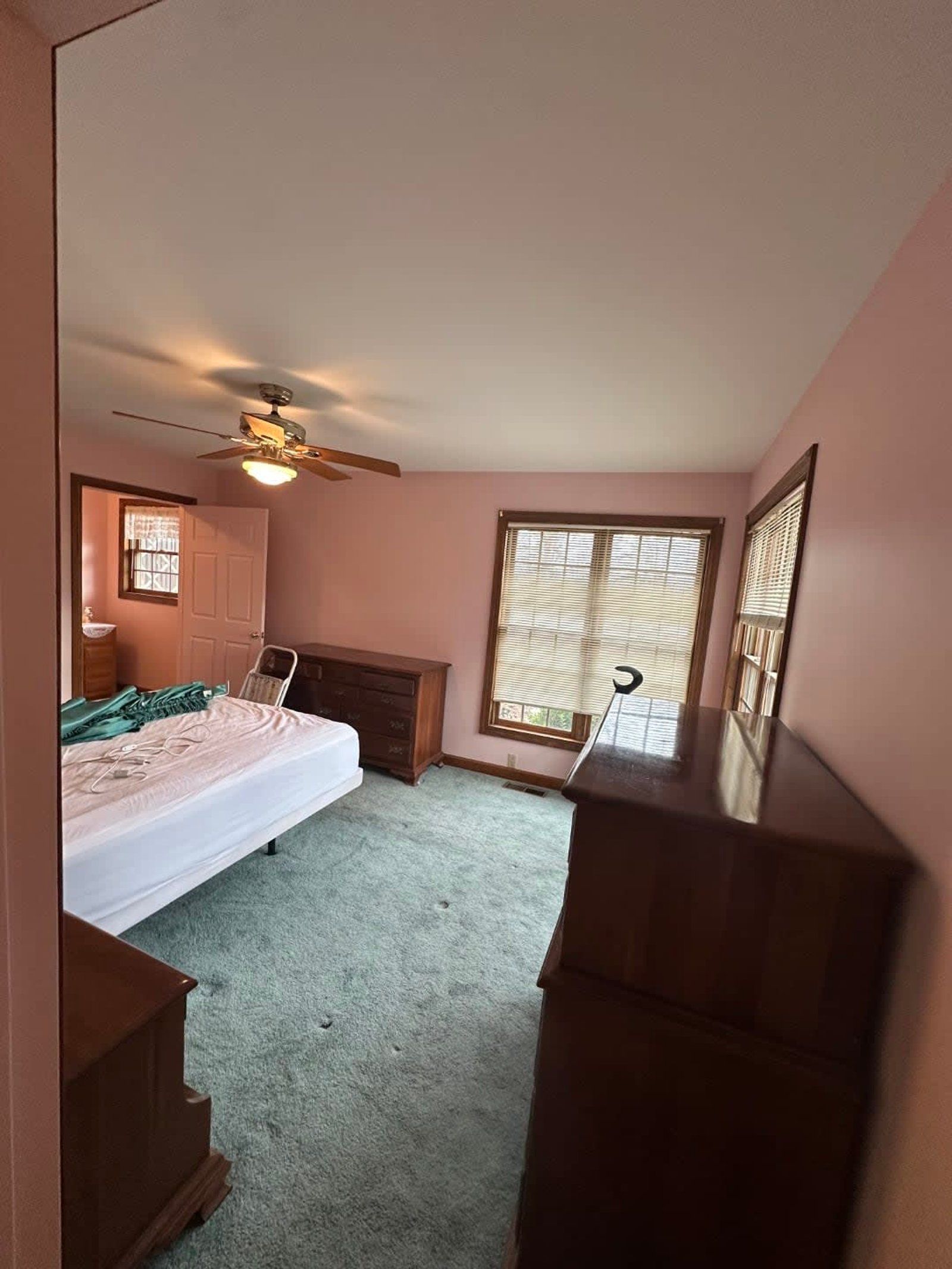 Bedroom with pink walls, green carpet, and wooden furniture. A bed and a window are visible.