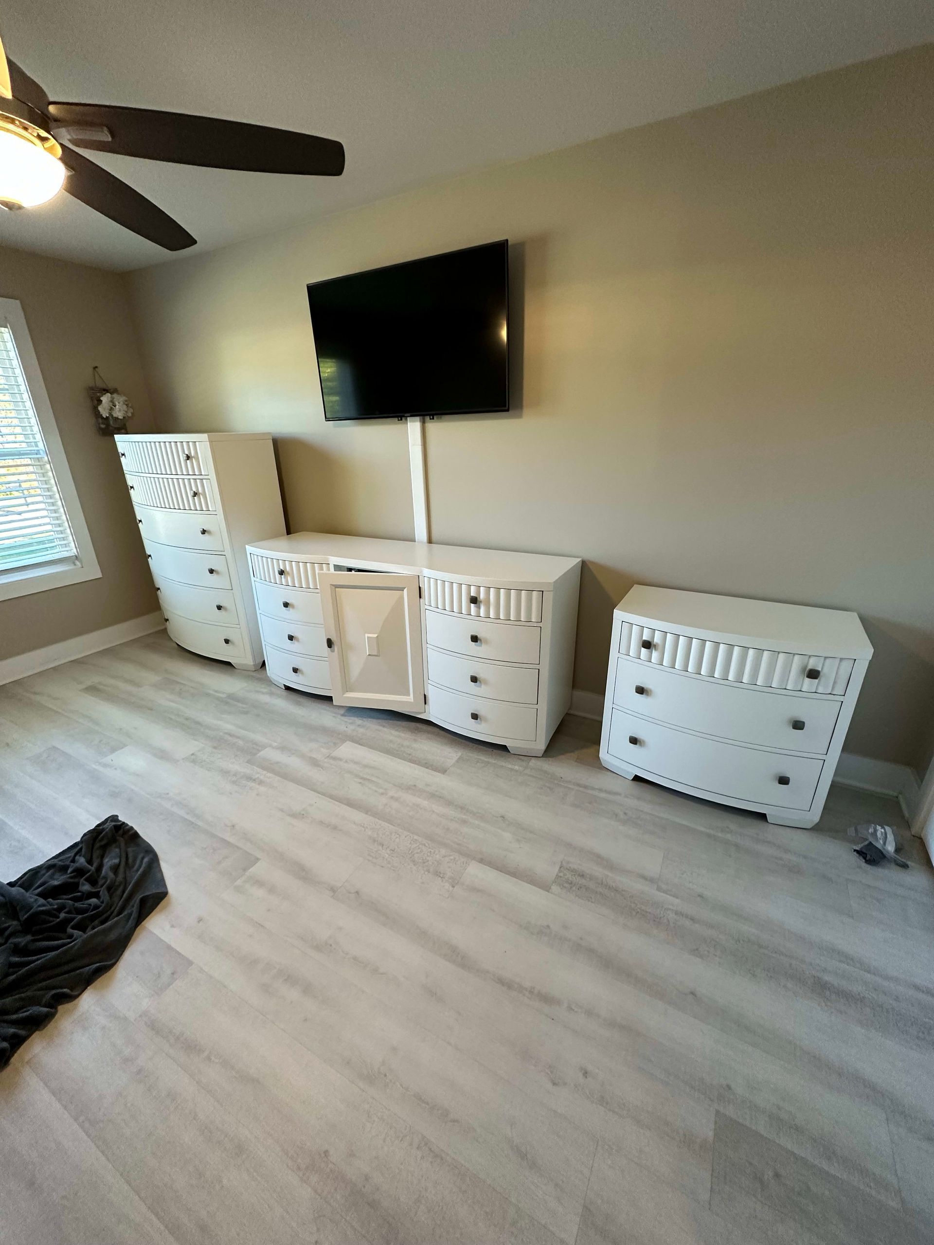 Bedroom with white dressers, TV on wall, ceiling fan, and light wood-look flooring.