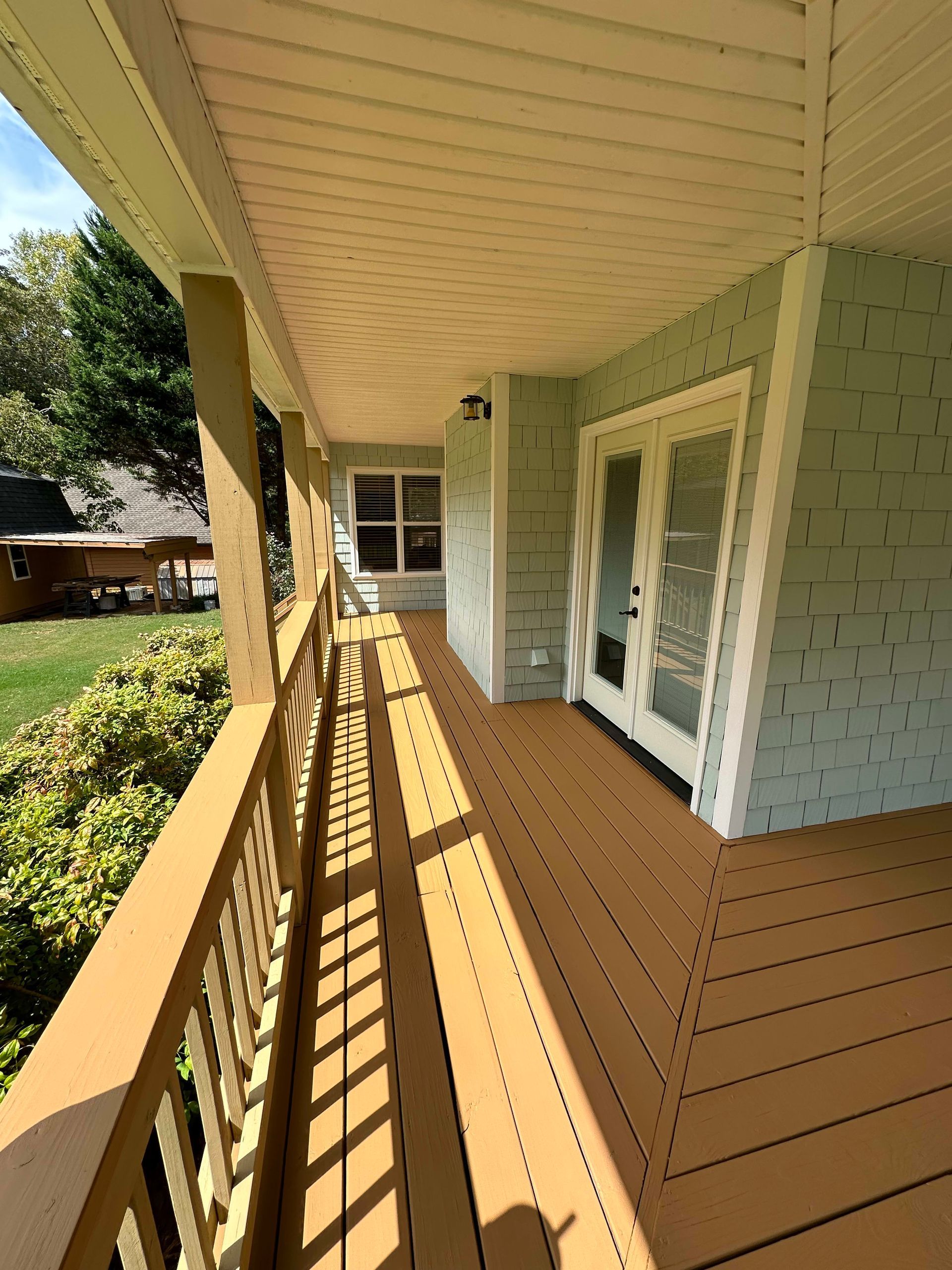 Covered porch with wood railing, tan floor, and light blue siding. Double doors lead inside.