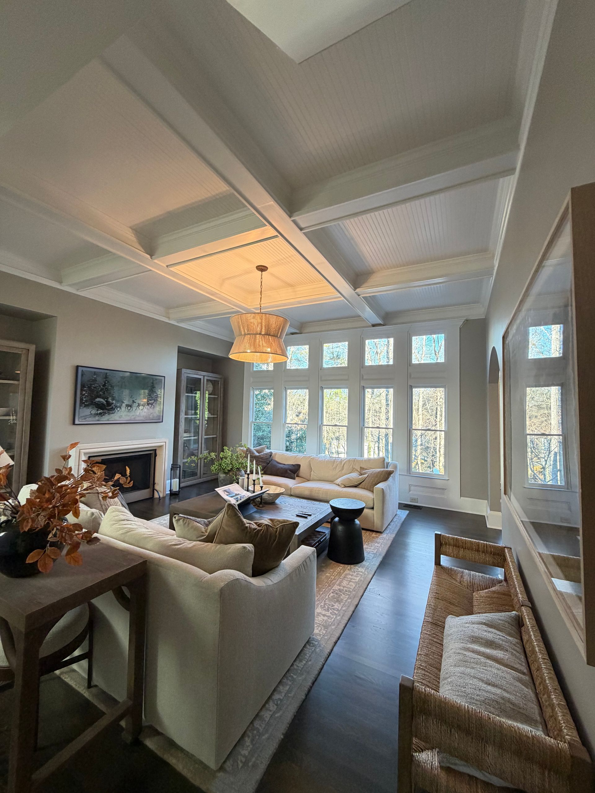 Elegant living room with cream sofa, fireplace, and large windows. Dark wood floors, chandelier, and a neutral color palette.