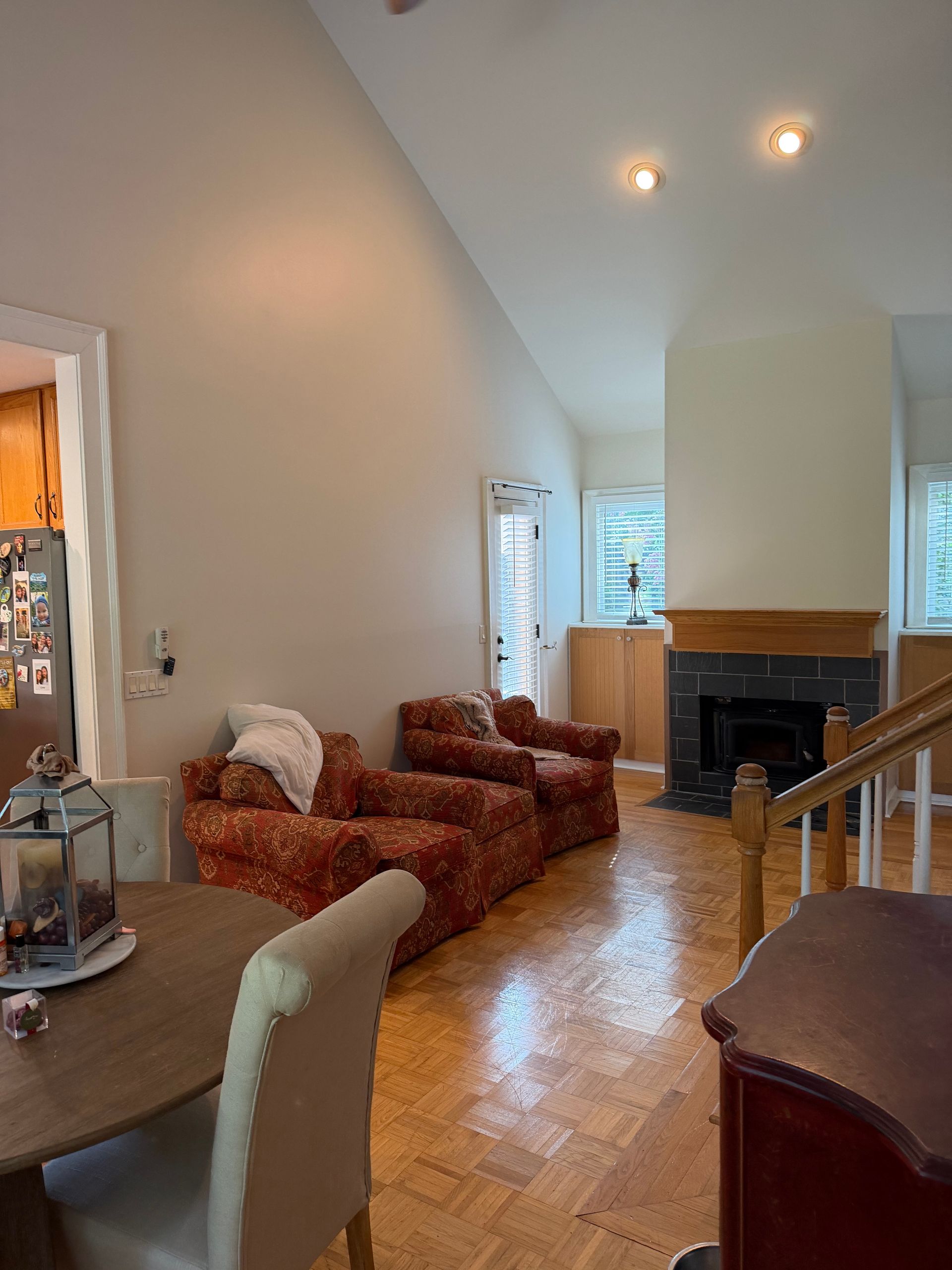 Living room with patterned chairs, hardwood floor, fireplace, and sloped ceiling with recessed lights
