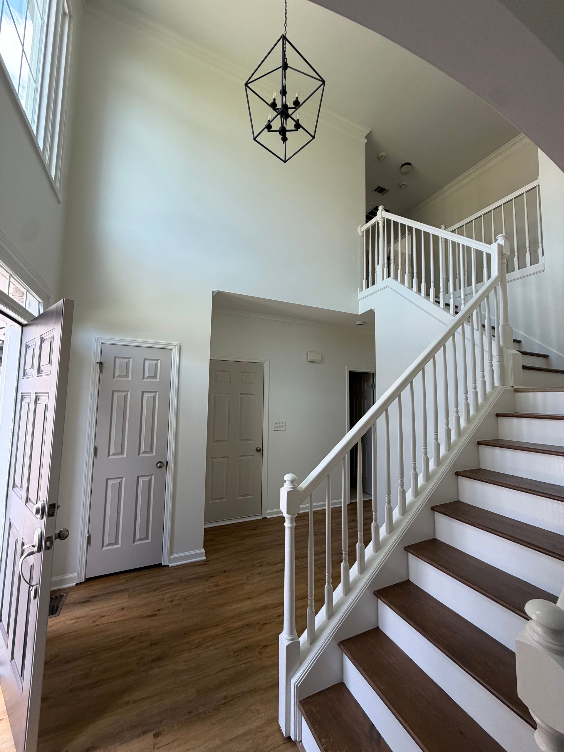 Bright foyer with staircase, white railings, wood floor, and hanging geometric light fixture