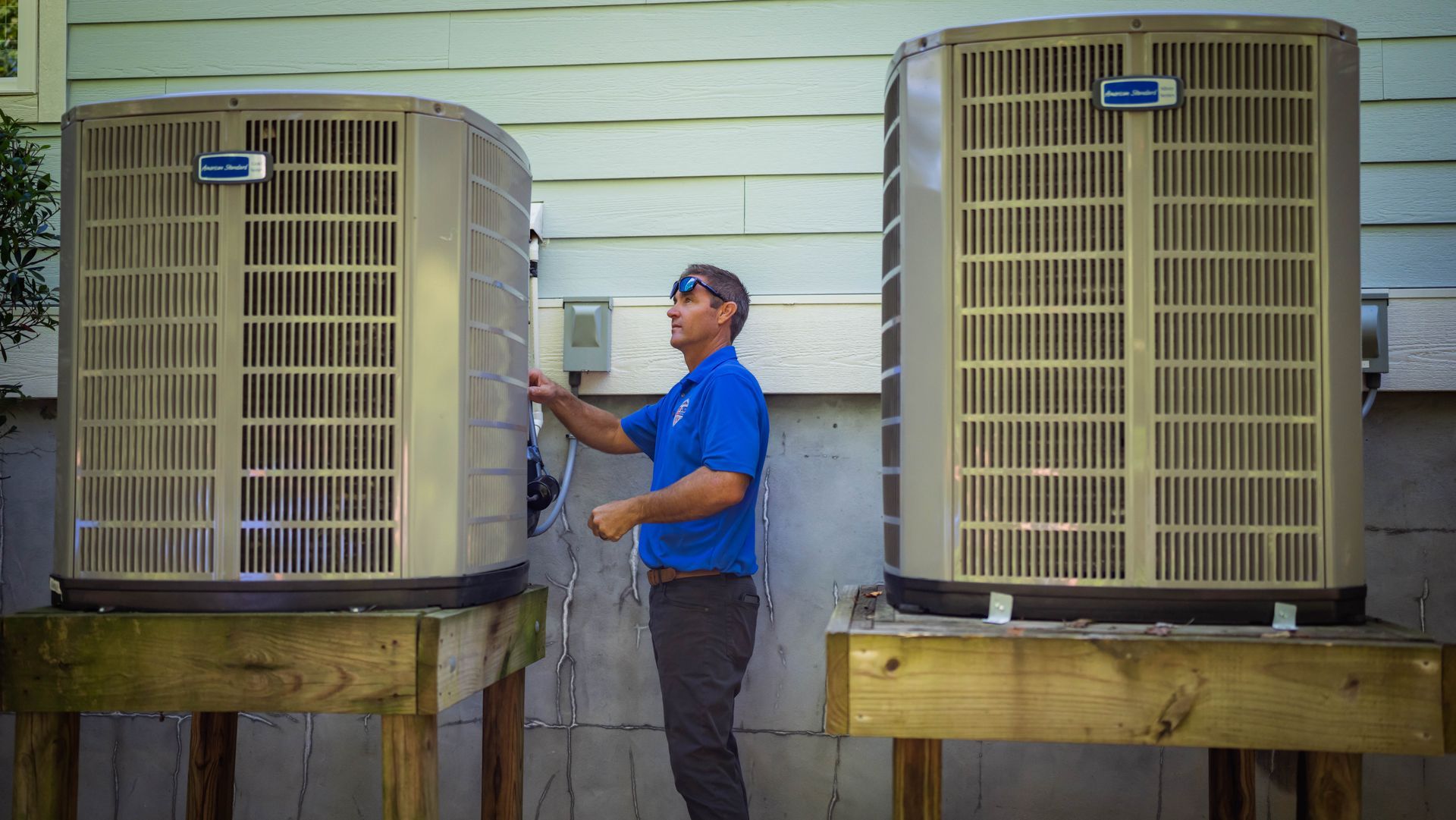Man inspecting two outdoor air conditioning units on wooden platforms.