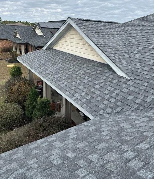 Gray shingle roofs on suburban homes with dormers and beige siding under a cloudy sky