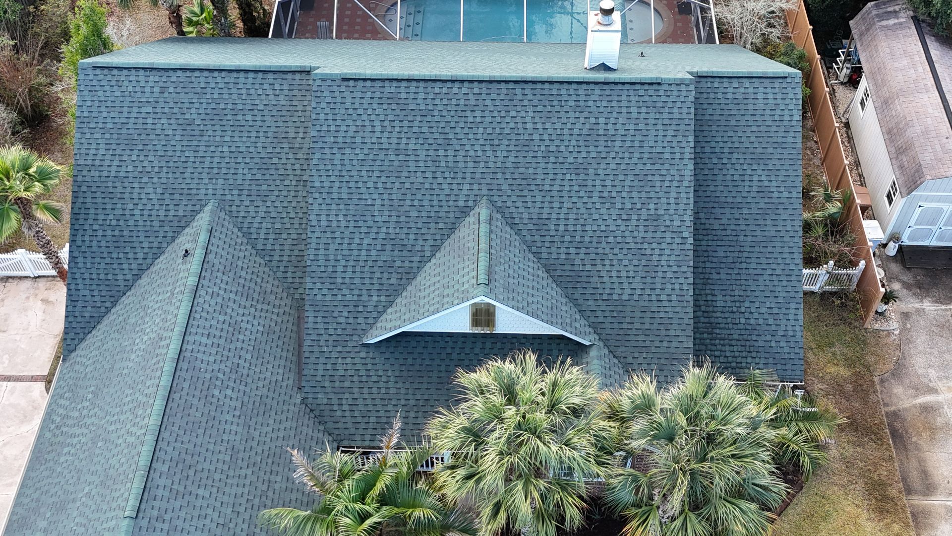 Overhead view of a house with a dark gray shingled roof, a chimney, and palm trees.