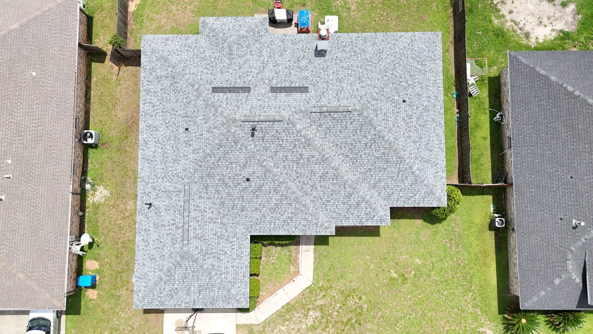 Aerial view of a gray-roofed house with a small yard and neighboring roofs.