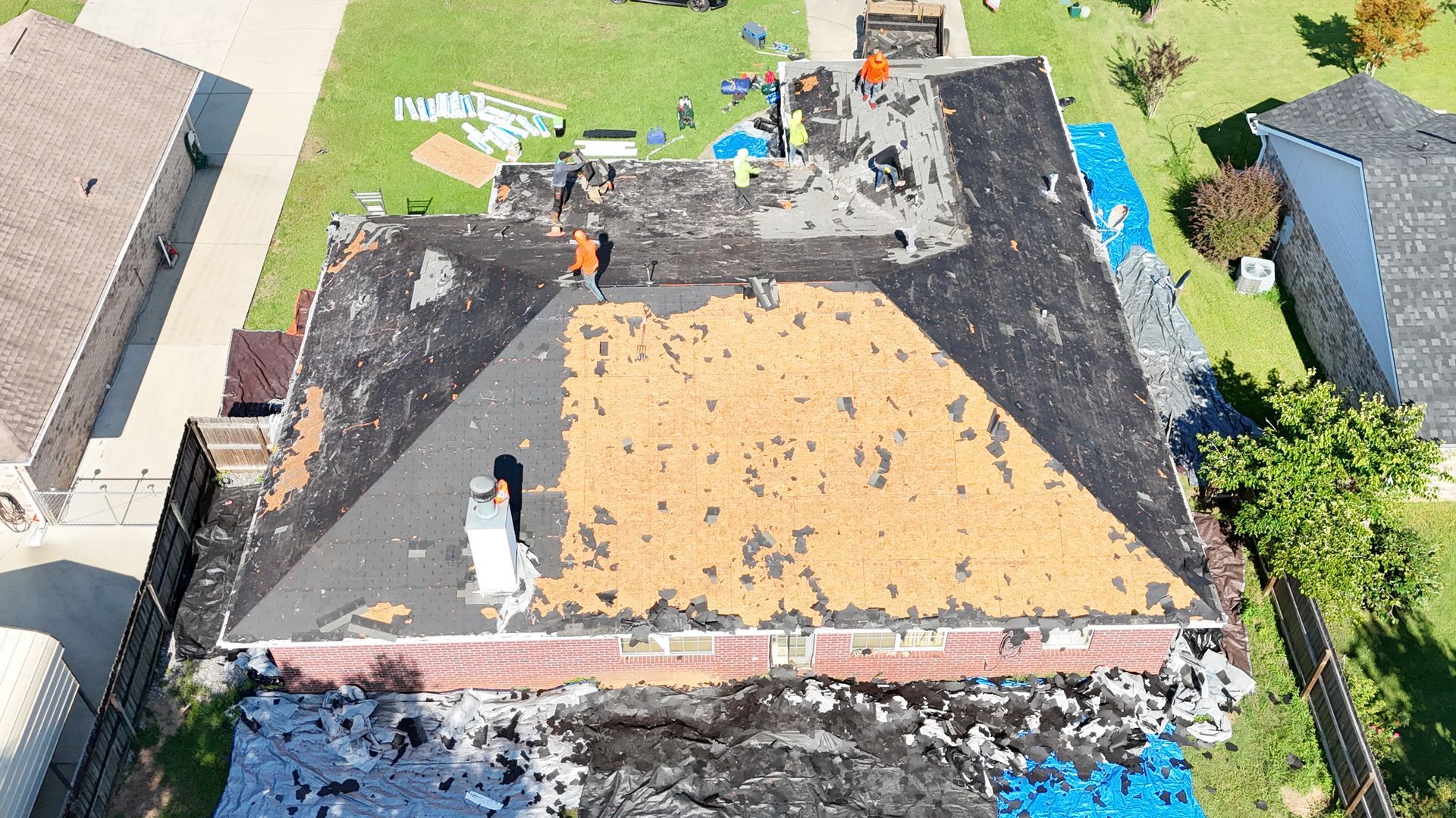 Aerial view of roof repair with exposed plywood and workers on a house roof
