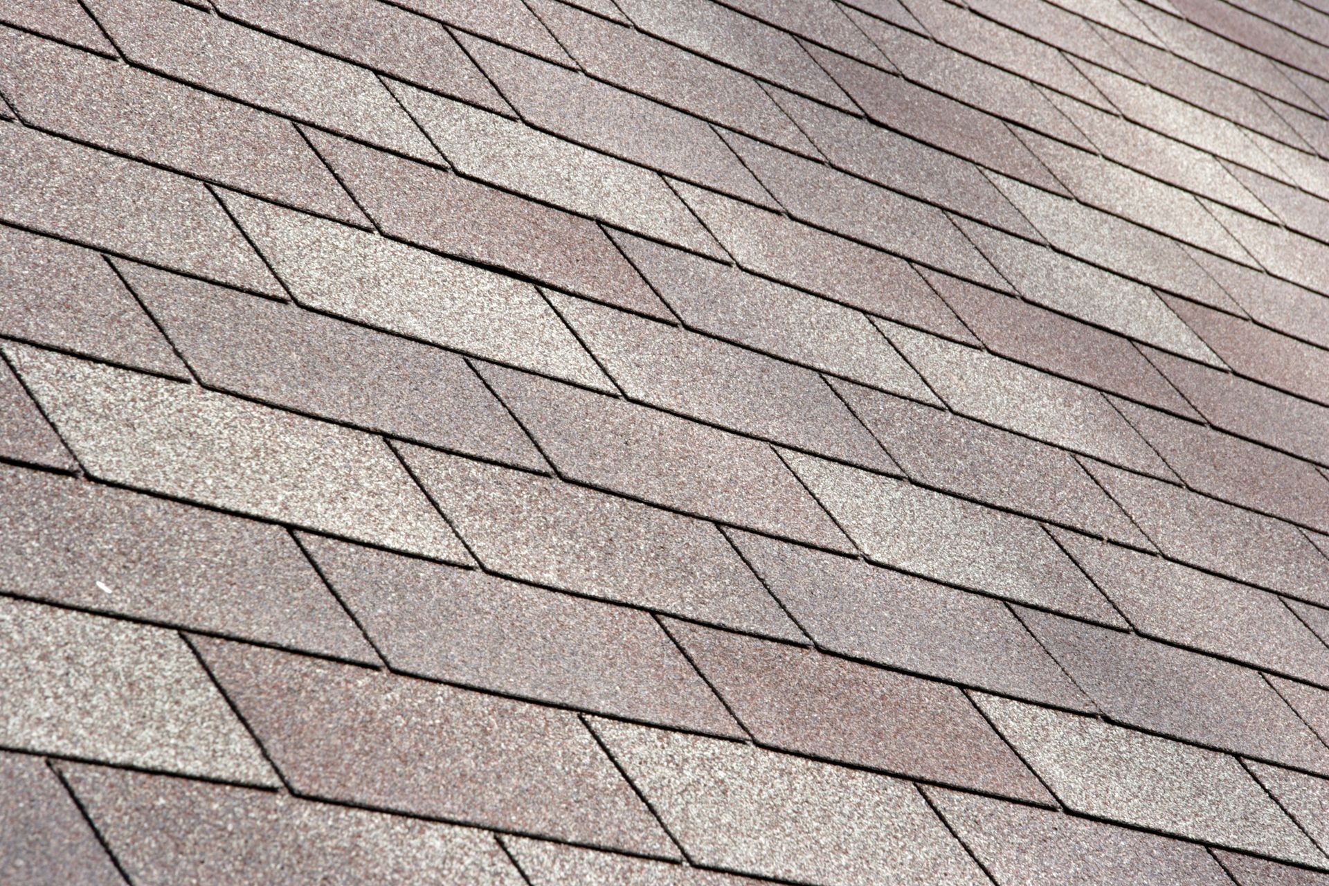 Close-up of a roof covered with overlapping diamond-shaped asphalt shingles in various shades of brown and gray.