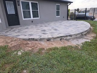 A gray paver patio with a curved edge next to a building and grass.