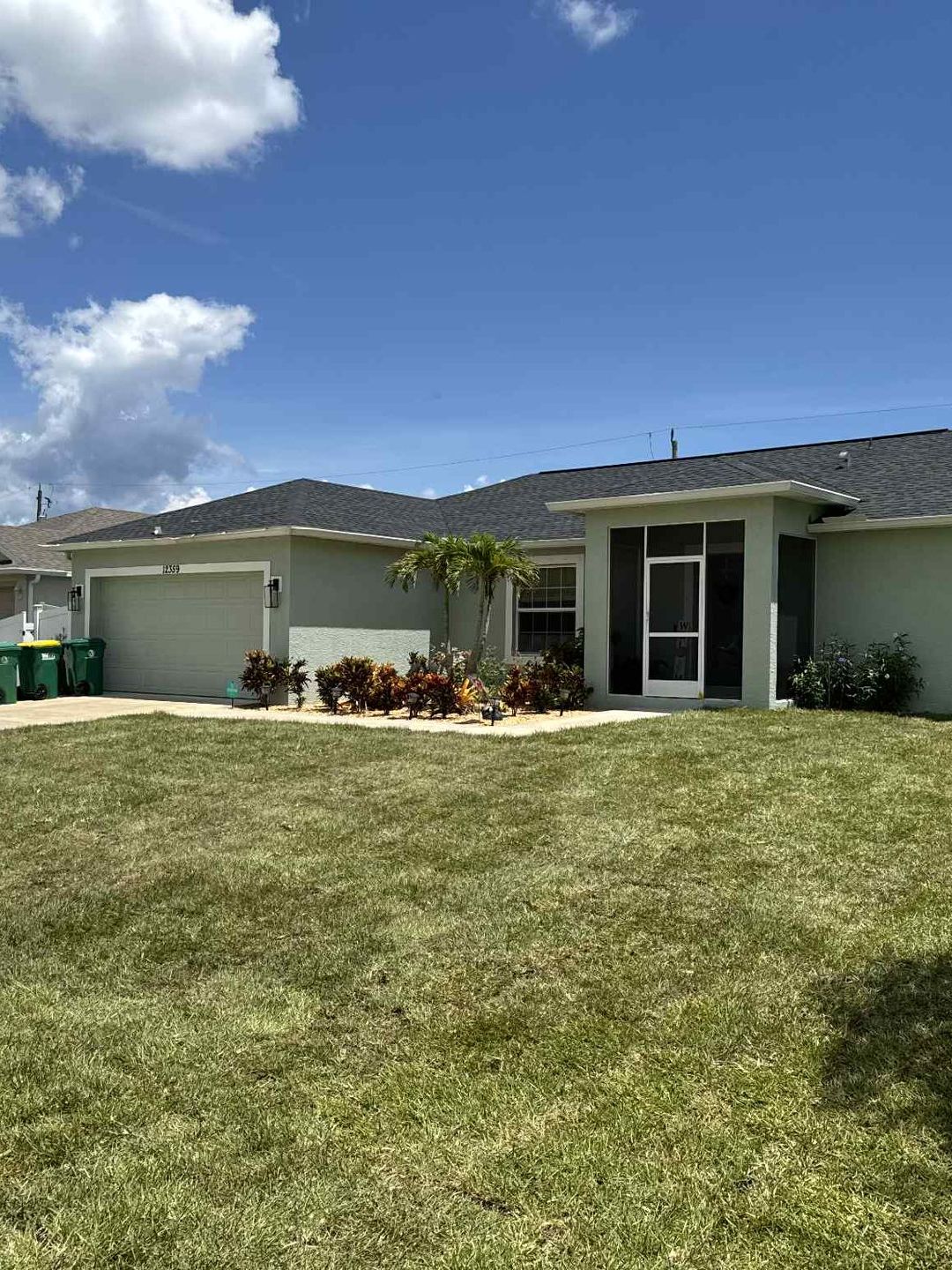 Green house with a garage and screened entryway; blue sky, green lawn.