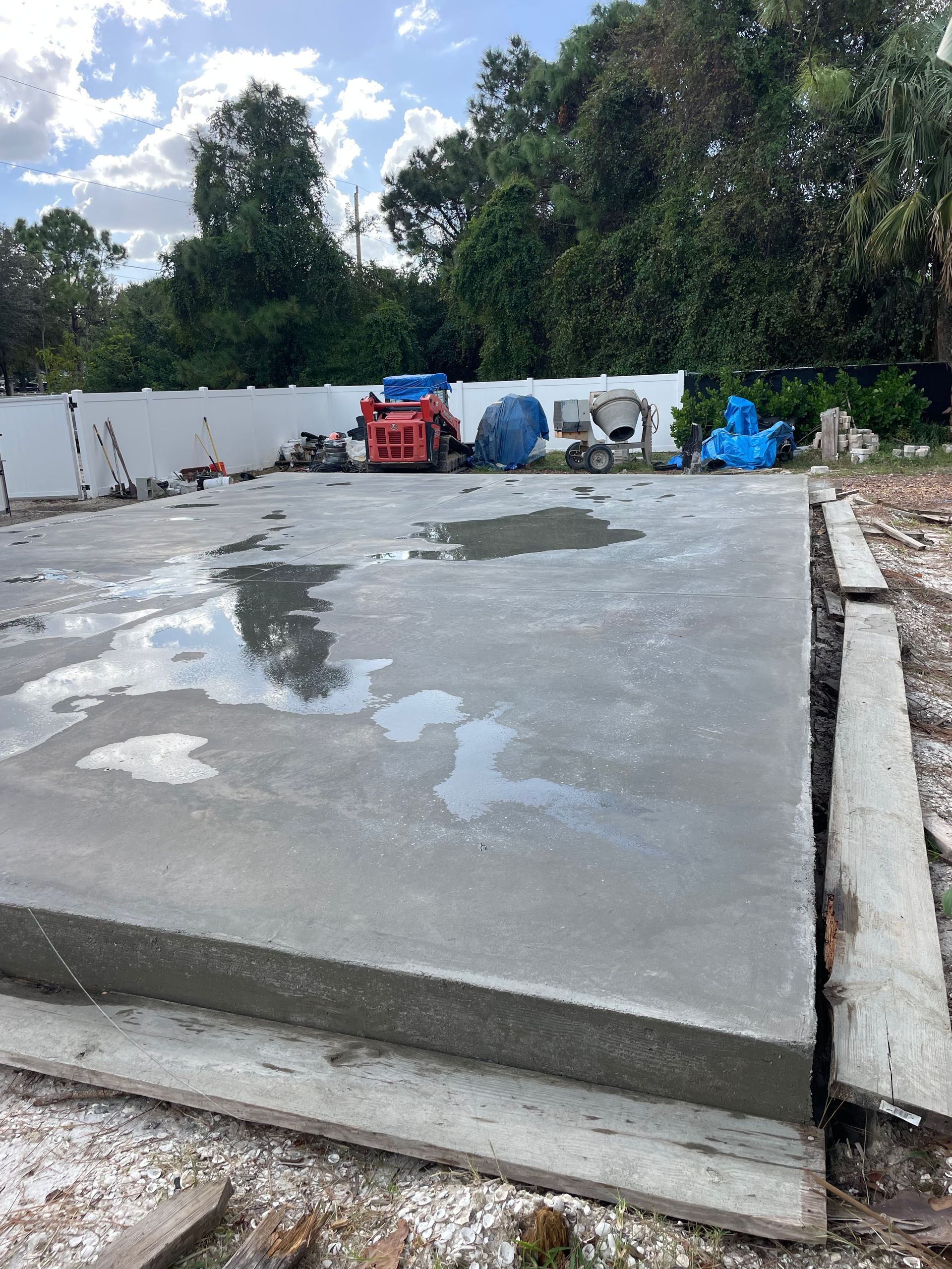 Newly poured concrete slab, wet with puddles, ready for construction. Tools and equipment in the background.