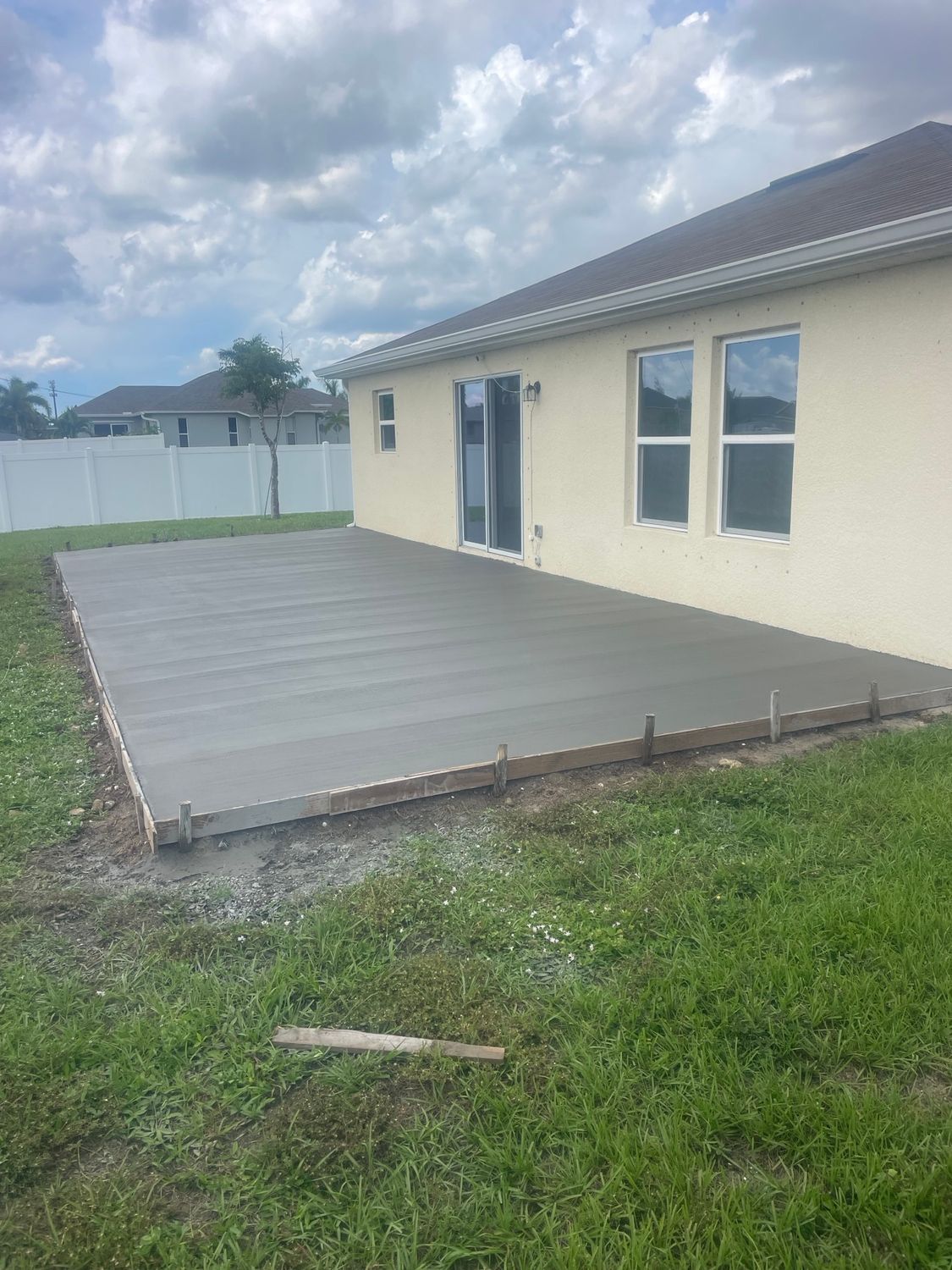 A freshly poured concrete patio outside a beige house on a green lawn.