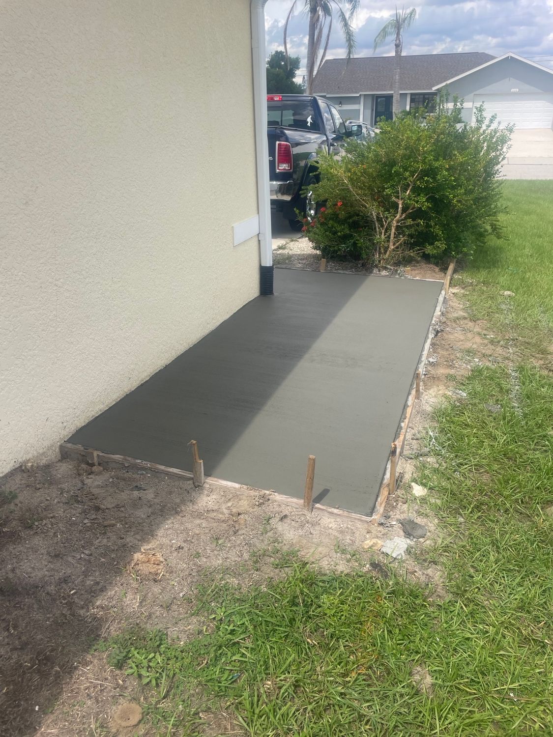 Freshly poured concrete walkway next to a house, surrounded by grass and a bush.