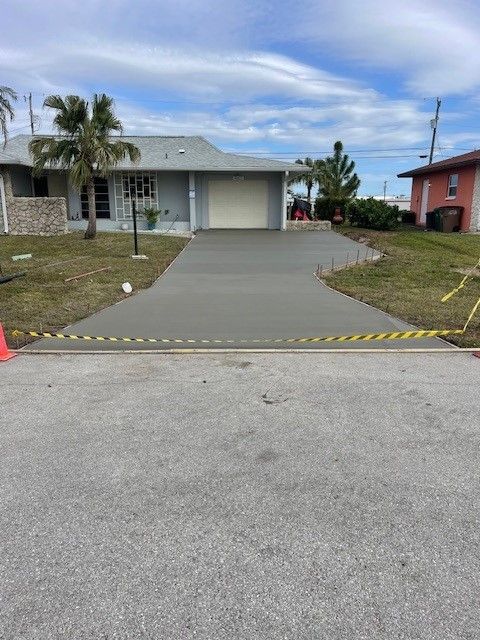 Newly poured concrete driveway in front of a light blue house with palm trees in the background.