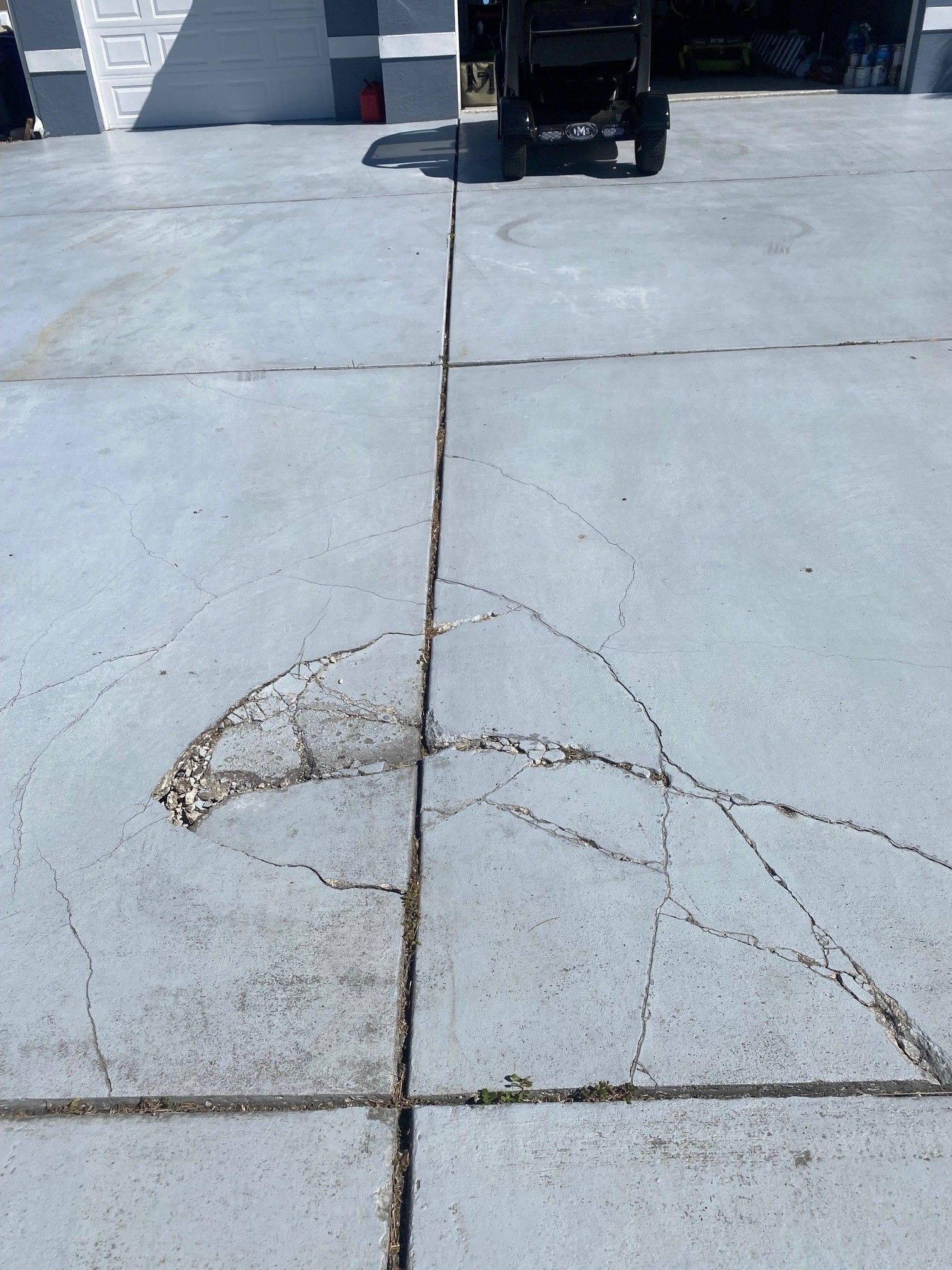 A concrete driveway with a large, cracked, and chipped section near a vertical control joint.