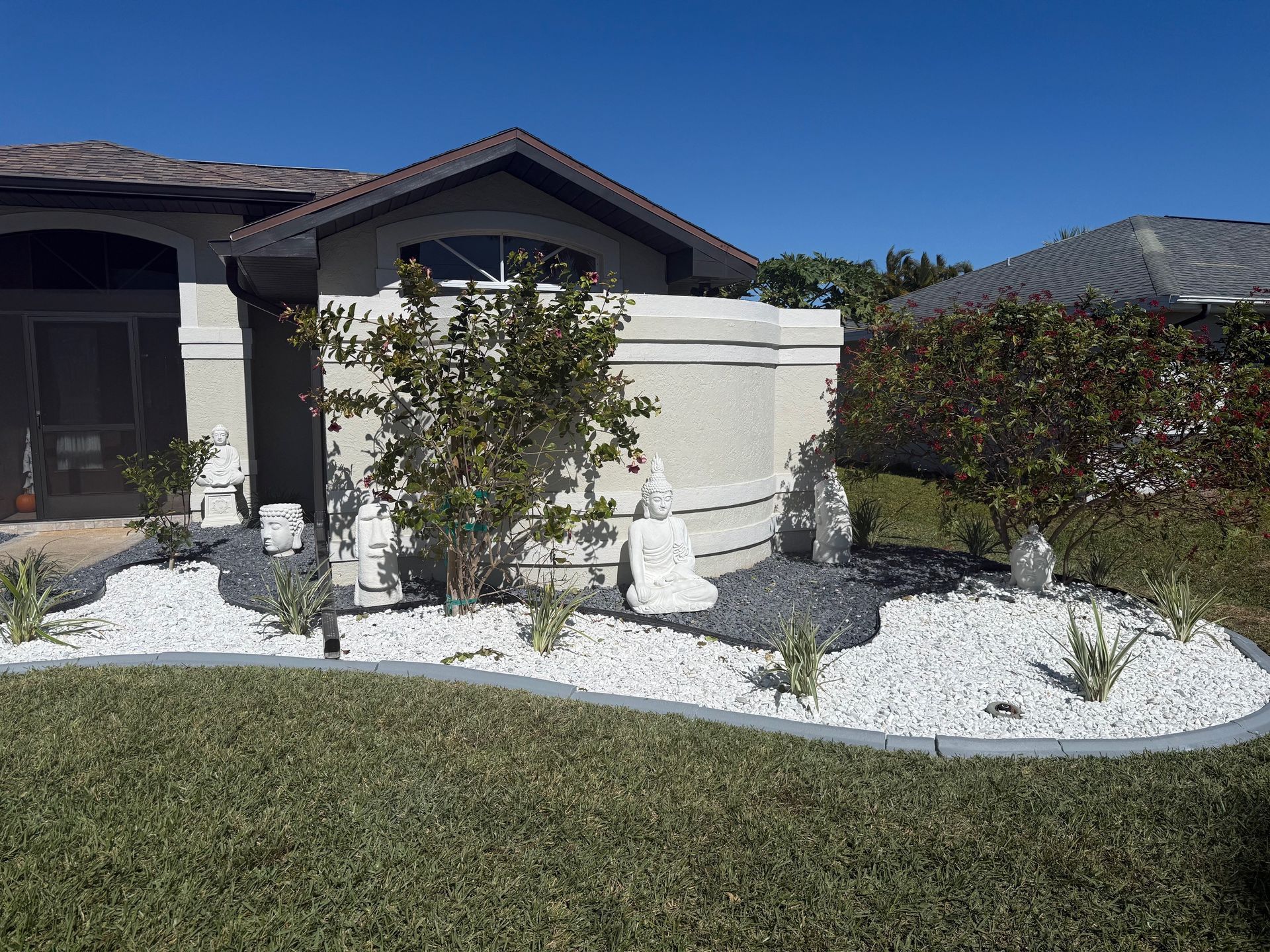 Landscaped front yard with white and gray rocks, green shrubs, and a house with a brown roof.