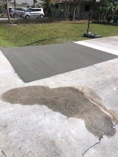 Gray concrete basketball court section on driveway, with a wet stain below.