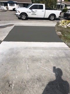 Concrete driveway with a new gray concrete patch, white pickup truck parked in the background.