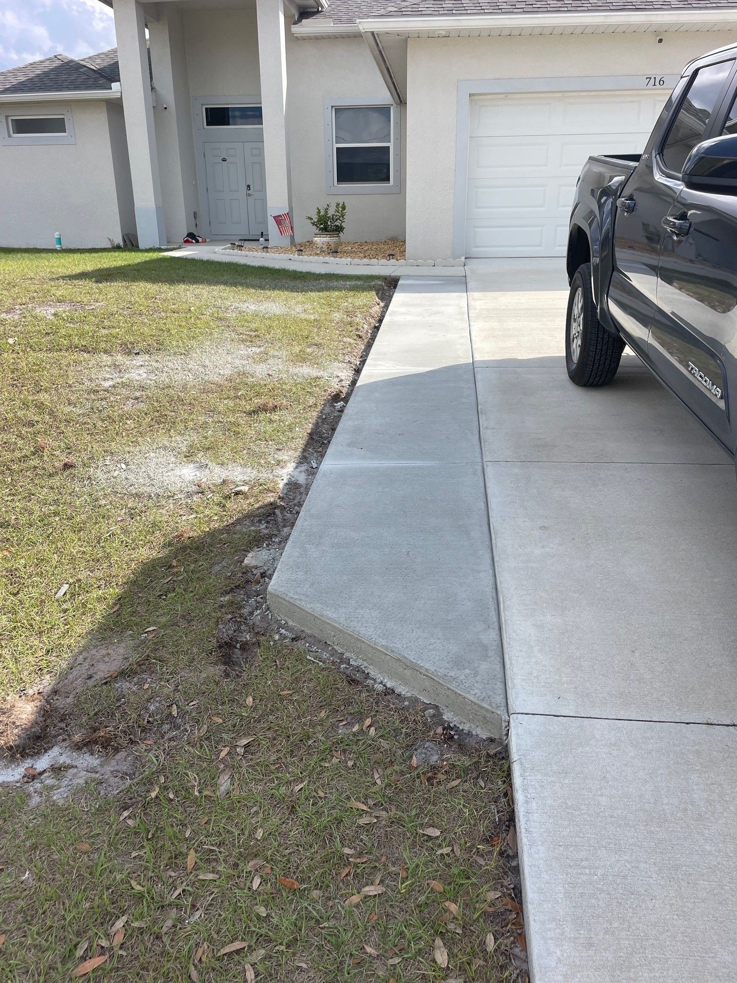 A concrete walkway addition adjacent to a driveway leads toward the front entrance of a house.