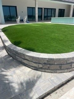 Curved retaining wall with artificial turf lawn and gray patio. Modern home exterior.