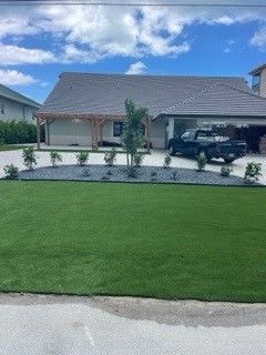 House with green lawn, gravel landscaping, and a black pickup truck parked in the driveway under a blue sky.